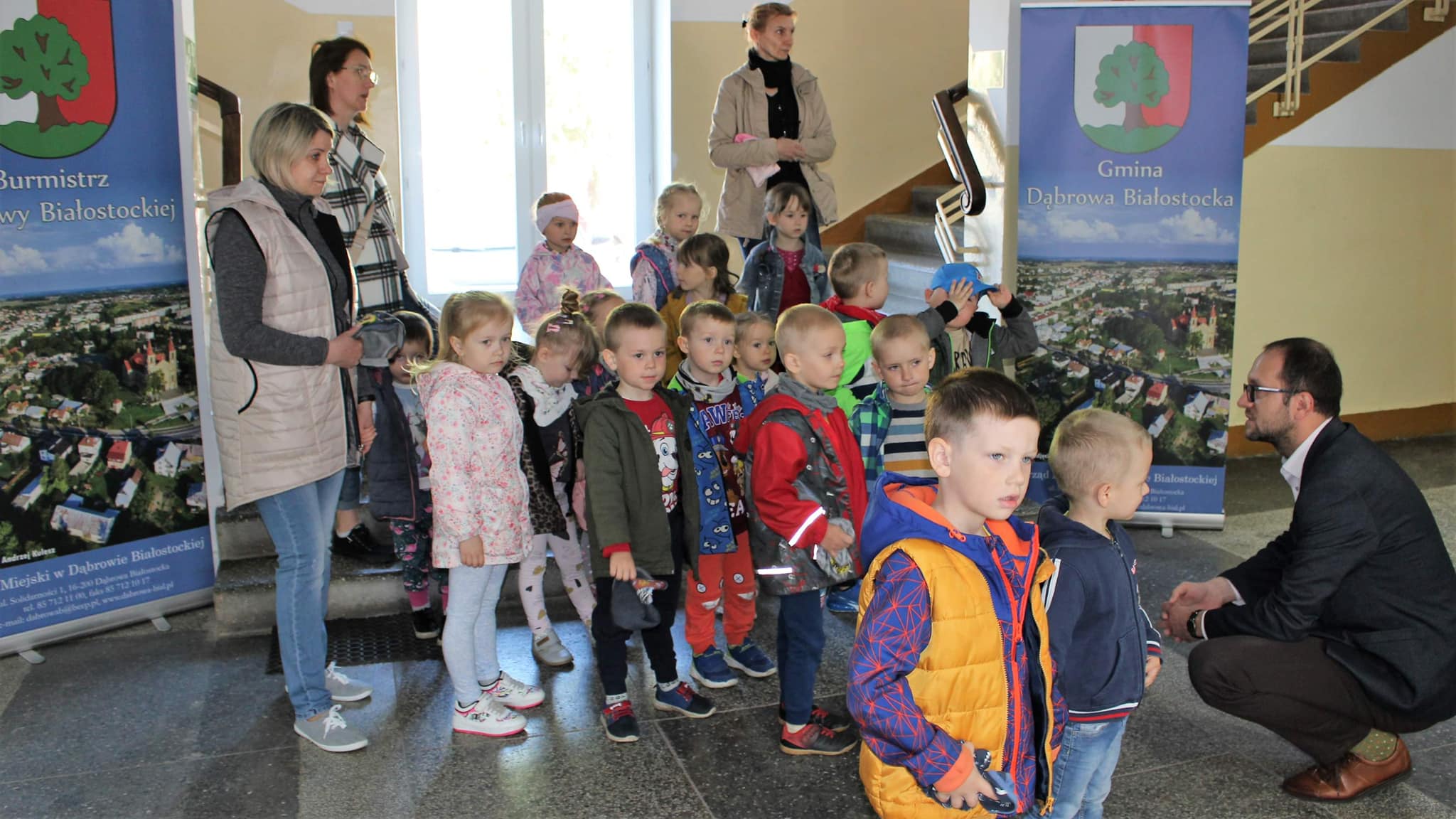 Burmistrz Dąbrowy Białostockiej na kucaka wita przedzkolaków w holu urzędu miejskiego
