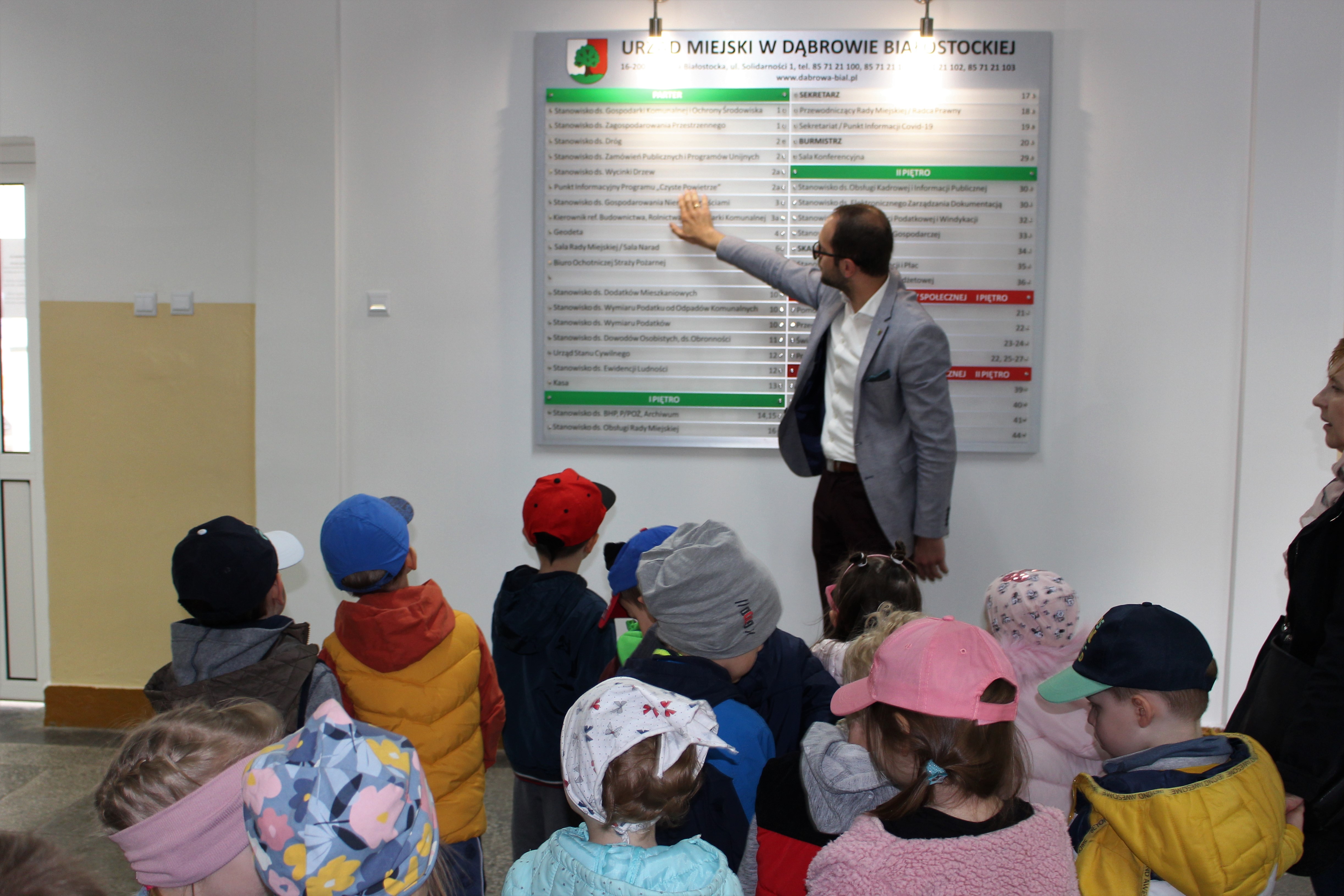 burmistrz dąbrowy białostockiej pokazuje przedszkolakom tablicę w korytarzu urzędu
