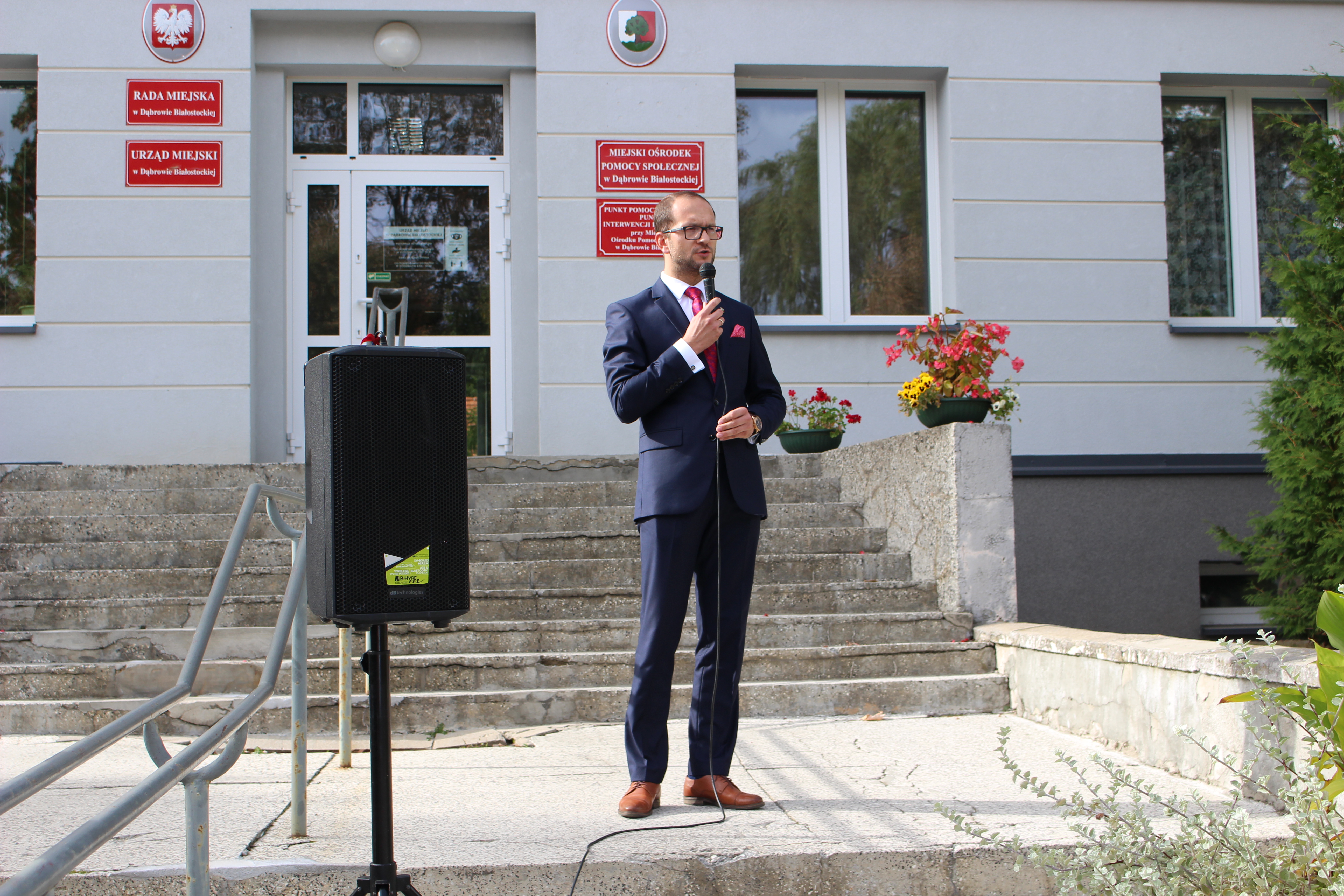 Burmistrz Dąbrowy Białostockiej przemawia do zgromadzonych w tle budynek urzędu
